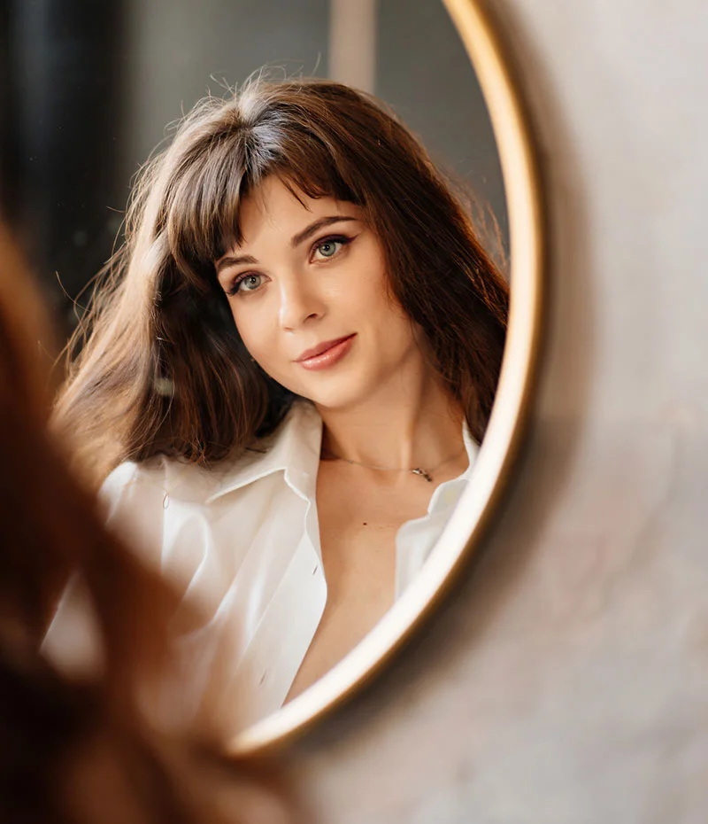 Brunette woman looking in a round mirror